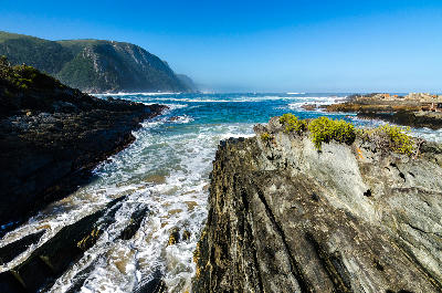 Rocky shoreline and surf beneath forested cliffs along the Tsitsikamma Coast in South Africa.