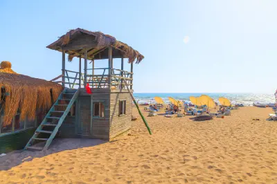 Wooden lifeguard tower on the golden sands of Patara Beach, with yellow umbrellas, sun loungers and beachgoers beside the Mediterranean Sea.