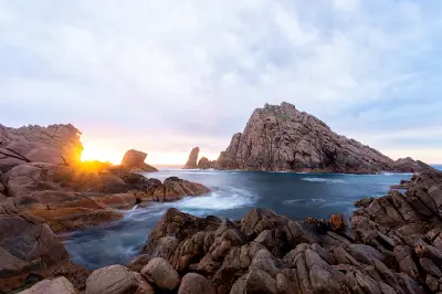 Sugarloaf Rock and surrounding jagged granite formations at sunset, with waves flowing through the rocky coastline at Cape Naturaliste, Western Australia.