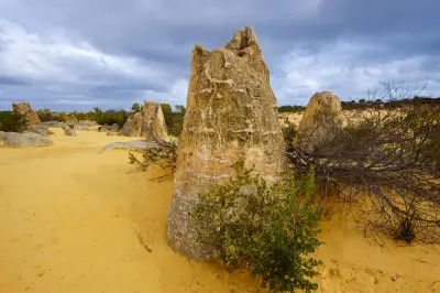 Large weathered limestone pinnacle rising from yellow sand and low vegetation beneath a cloudy sky.