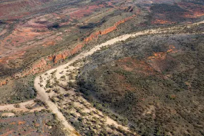 Aerial view of a dry creek bed winding between parallel rocky ridges in the West MacDonnell Ranges.