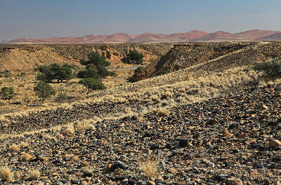 Rocky desert landscape and shallow canyon terrain near Sesriem with distant Namib Desert dunes in Namibia.
