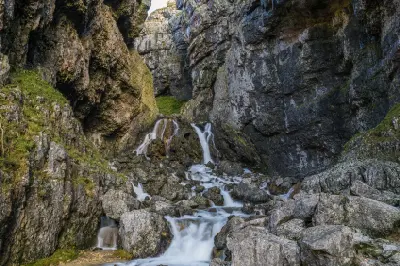 Cascading waterfalls flowing over limestone boulders between steep rock walls inside Gordale Scar, North Yorkshire.