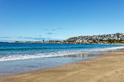 View from Santos Beach in Mossel Bay showing the calm shoreline, harbour breakwater and coastal townscape overlooking the sheltered waters of the bay.