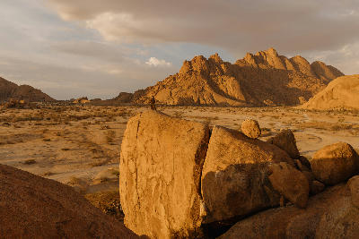 Photographer standing on granite boulders at sunset beneath the Spitzkoppe mountain formations in Namibia.