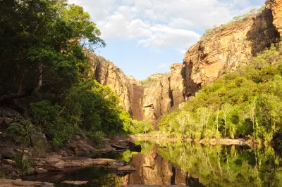 Still plunge pool reflecting towering golden sandstone cliffs and dense green vegetation at Jim Jim Falls in Kakadu National Park, Northern Territory, Australia.