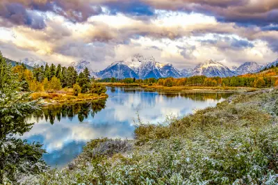 Oxbow Bend reflecting the Teton Range with autumn trees and fresh snow under dramatic clouds, Grand Teton National Park, Wyoming.