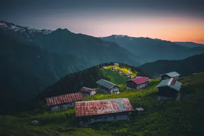 Wooden houses scattered across Pokut Plateau beneath the Kaçkar Mountains during a colourful summer sunrise in Rize, Turkey.