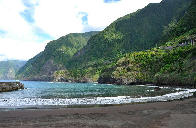 Black sand beach and steep green cliffs at Seixal on the north coast of Madeira Island, Portugal.
