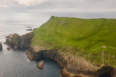 Wide aerial view of Mykines Hólmur Lighthouse and steep Atlantic cliffs on Mykines island, Faroe Islands.