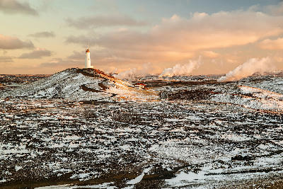 Winter sunrise over Reykjanesviti lighthouse with snow-dusted volcanic landscape and geothermal steam on the Reykjanes Peninsula, Iceland.