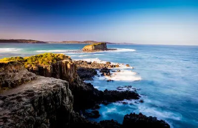 Rugged coastal cliffs and an offshore rock formation surrounded by blue ocean water near Minnamurra on the Illawarra Coast.