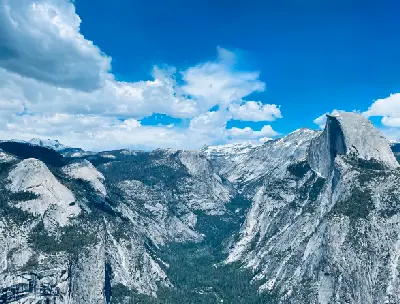 View from Glacier Point in Yosemite National Park showing Half Dome, granite cliffs, and Yosemite Valley beneath a blue sky with clouds.