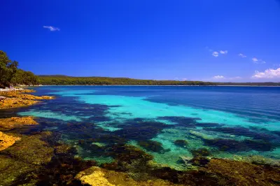 Clear turquoise shallows reveal rocky reef beneath the water along the bush-fringed shoreline of Hyams Beach in Jervis Bay.