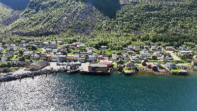 Aerial view of Gryllefjord waterfront with houses and shoreline buildings beneath steep mountain slopes