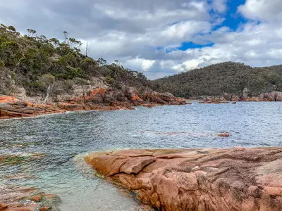 Sheltered waters bordered by pink granite rocks and forest at Sleepy Bay, Freycinet National Park, Tasmania.