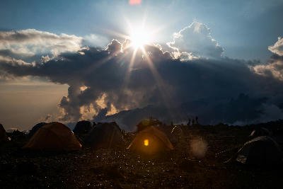 Camping tents at Shira Camp on Mount Kilimanjaro, Tanzania, with sunlight breaking through dramatic clouds at approximately 3,850 metres above sea level.