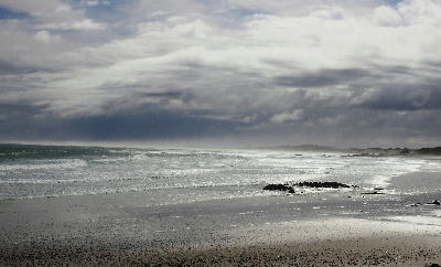 Dark storm clouds above Sixteen Mile Beach with wind-driven Atlantic surf, wet sand and sea mist stretching along the West Coast near Yzerfontein.