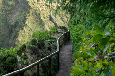 Narrow hiking path with wooden railing along a steep green slope on São Miguel Island, leading toward the Miradouro da Boca do Inferno viewpoint in the Azores.