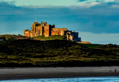 Bamburgh Castle catches the warm evening light beneath dramatic storm clouds, viewed across the Northumberland coast near Seahouses.