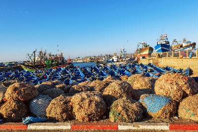 Blue fishing boats and piled fishing nets inside the busy harbour of Essaouira in Atlantic Morocco.