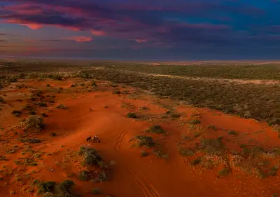 Horse riders cross the red earth of Bullara Station beneath a dramatic sunset sky near Exmouth Gulf.