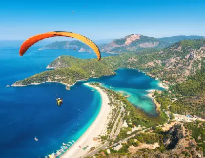 Paraglider flying above Ölüdeniz Blue Lagoon, beach and turquoise Mediterranean coast in Türkiye.