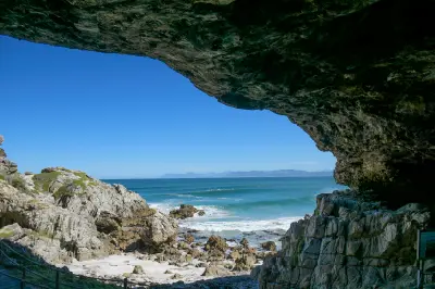 View from inside Klipgat Cave looking out across rocky shoreline, ocean waves, and coastal cliffs near De Kelders in Walker Bay, South Africa.
