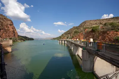 View along the Hartbeespoort Dam wall with calm reservoir waters stretching into the distance between steep rocky hills of the Magaliesberg mountain range in North West Province, South Africa.