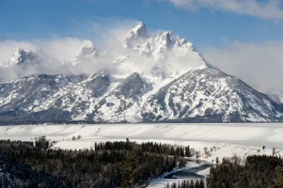 Winter view of the Grand Teton Range with snow-covered peaks, frozen river, and forest in Wyoming.