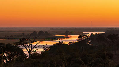 Panoramic sunset over the Kwando River floodplain with winding waterways and silhouetted trees in the Linyanti region of Botswana.