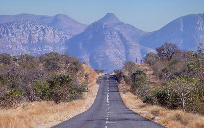 Two-lane road running through dry bushveld towards the rugged cliffs and peaks of Abel Erasmus Pass in Limpopo Province, South Africa.