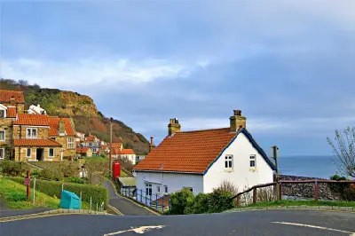Stone cottages with red-tiled roofs along a narrow village street in Runswick Bay, with a grassy hillside and the North Sea in the background.