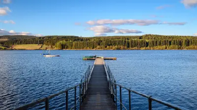 Wooden jetty leading into Kielder Water in Northumberland, with small boats on the blue reservoir and forested hills beneath a partly cloudy sky.
