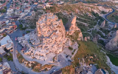 Aerial view of Uçhisar Castle in Cappadocia, Turkey, showing rock-cut chambers, surrounding village and volcanic landscape.