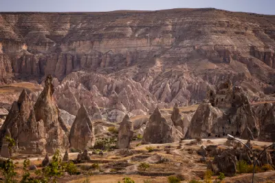 Panoramic landscape of Cappadocia featuring fairy chimneys, volcanic rock formations and ancient cave dwellings beneath layered cliffs in Central Anatolia, Turkey.