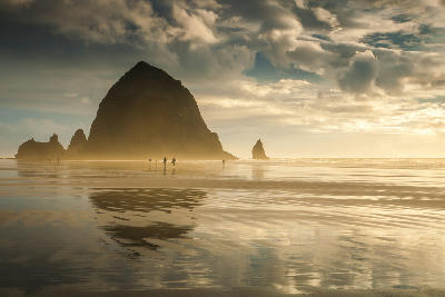 Haystack Rock at Cannon Beach Oregon USA at sunset with reflections and people walking along the shoreline