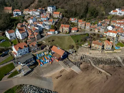 Elevated aerial view of colourful kayaks beside the beach, stone cottages with red-tiled roofs and narrow village streets in Runswick Bay, North Yorkshire, England.