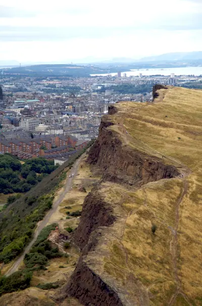 Salisbury Crags volcanic cliffs above Edinburgh with hikers walking along the ridge.