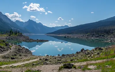 Medicine Lake with mountain reflections and small figures standing along the rocky shoreline