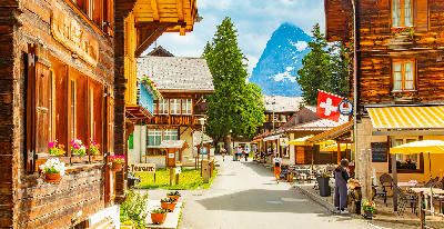 Pedestrian street in Mürren village lined with wooden chalets, flower boxes, and a Swiss flag, with alpine peaks visible in the background, Switzerland.