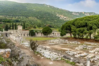 Wide view of the ancient ruins of Ephesus, with marble columns, scattered stone remains and monumental structures set against green hills near Selçuk, Turkey.
