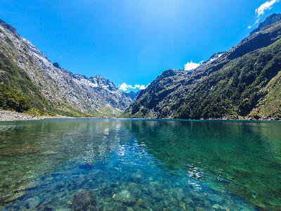 Clear turquoise waters of Lake Marian surrounded by steep alpine mountains in Fiordland National Park, South Island, New Zealand.