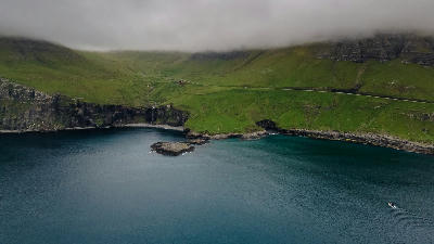Aerial coastal view of Skarðsáfossur waterfall descending into a sheltered Atlantic cove on Vágar Island, Faroe Islands.