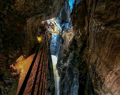 Visitors standing on a viewing platform inside Trümmelbach Falls, overlooking a narrow vertical gorge with rushing water between smooth rock walls in Lauterbrunnen Valley, Switzerland.