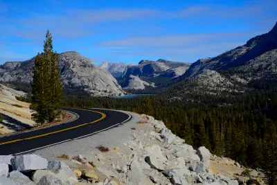 Curving Tioga Pass Road above Tenaya Lake with granite domes and forested alpine landscape in Yosemite National Park.