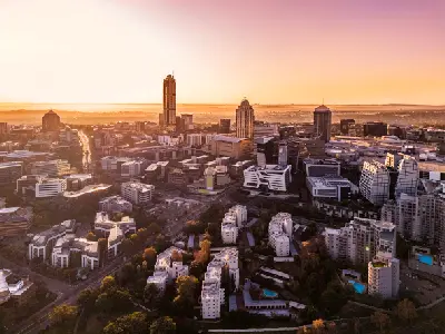 Aerial view of the Sandton skyline at sunrise in Johannesburg, Gauteng, South Africa, with modern office towers and commercial buildings bathed in golden morning light.