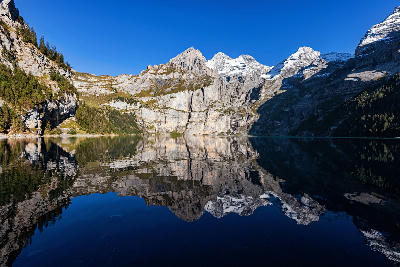 Oeschinensee reflecting steep cliffs, rocky slopes, and alpine peaks in calm water in the Bernese Alps, Switzerland.