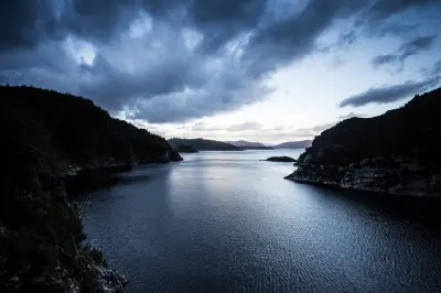 Lake Gordon surrounded by rugged forested mountains beneath dramatic clouds in southwest Tasmania, Australia.
