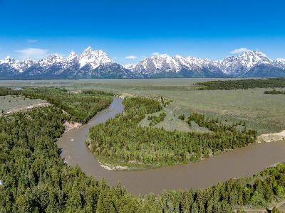 Aerial view of the Snake River curving through forest and open valley with the Teton Range in clear daylight, Wyoming.